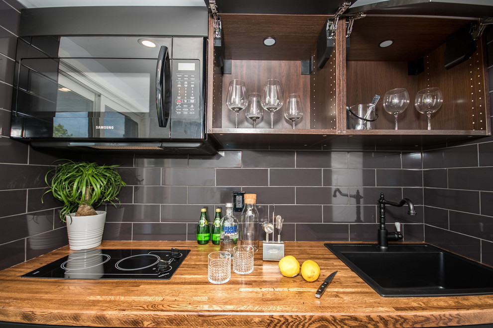 Photo of a small contemporary single-wall kitchen pantry in Toronto with a built-in sink, flat-panel cabinets, black cabinets, wood worktops, black splashback, ceramic splashback, black appliances, porcelain flooring, no island, grey floors and brown worktops.
