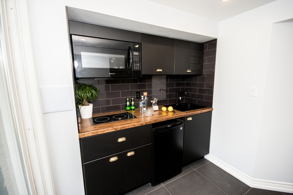 Inspiration for a small contemporary single-wall kitchen pantry in Toronto with a built-in sink, flat-panel cabinets, black cabinets, wood worktops, black splashback, ceramic splashback, black appliances, porcelain flooring, no island, grey floors and brown worktops.