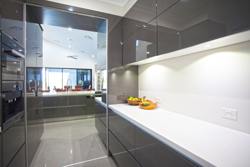 This is an example of a large modern galley kitchen pantry in Other with stainless steel appliances, an island, flat-panel cabinets, grey cabinets, granite worktops, ceramic flooring, grey floors and white worktops.
