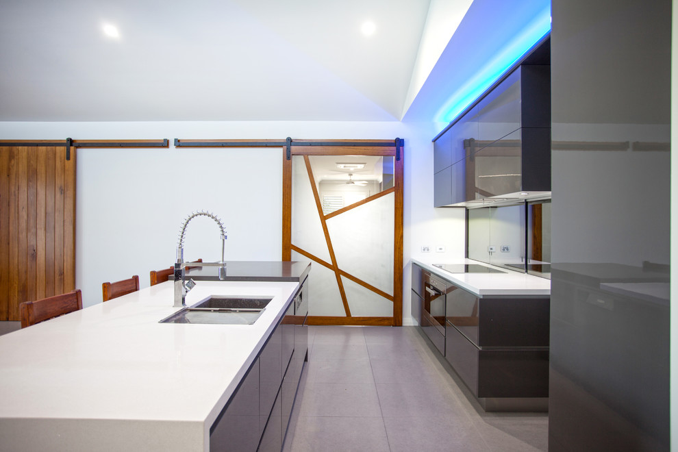 Foto på ett stort funkis vit kök, med en dubbel diskho, spegel som stänkskydd, rostfria vitvaror, en köksö, släta luckor, grå skåp, granitbänkskiva, klinkergolv i keramik och grått golv