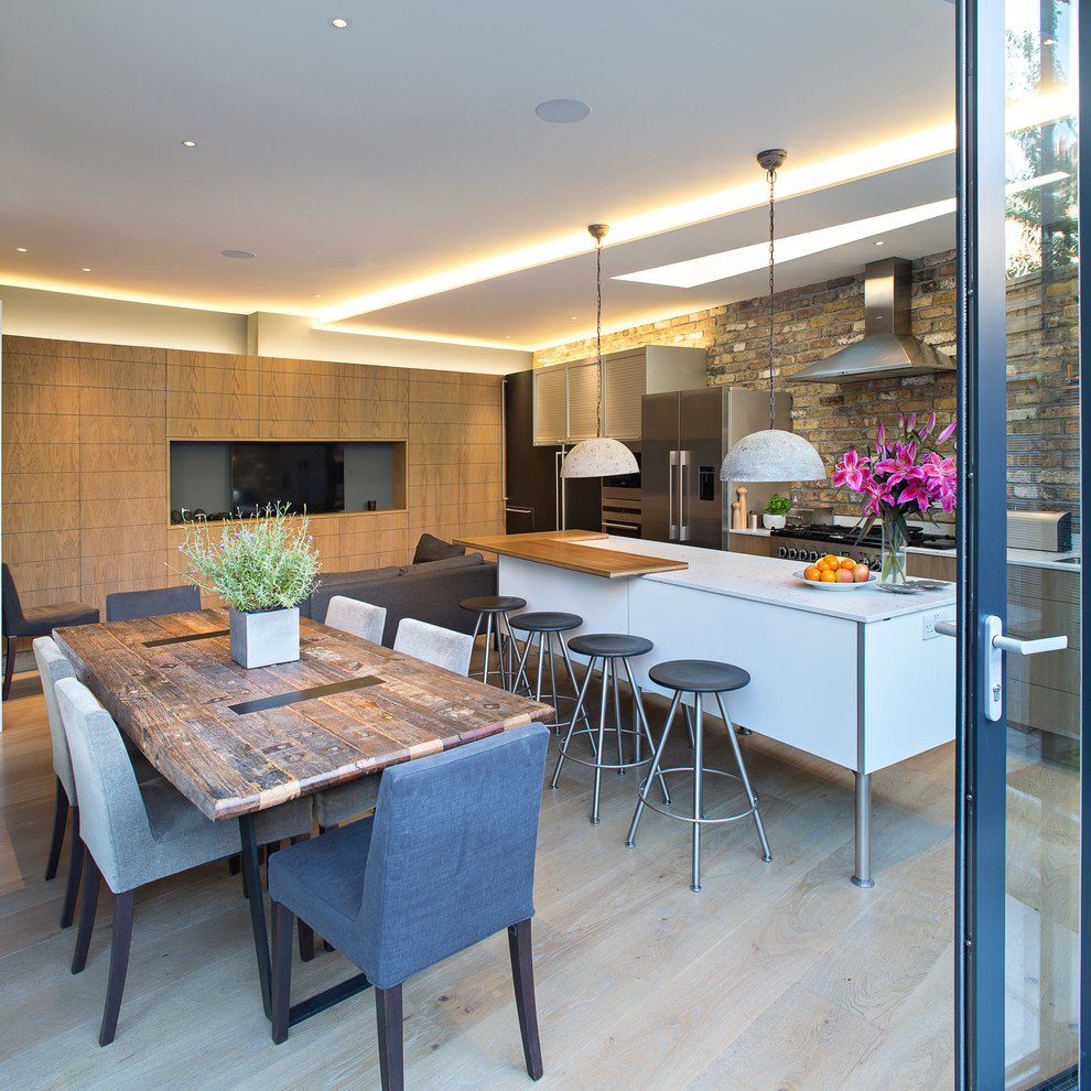 This is an example of a contemporary galley open plan kitchen in London with flat-panel cabinets, medium wood cabinets, stainless steel appliances, light hardwood flooring and an island.