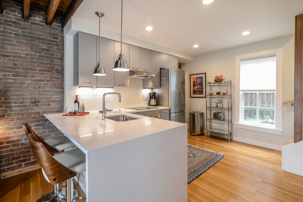 Inspiration for a small rustic l-shaped medium tone wood floor and brown floor eat-in kitchen remodel in Detroit with an undermount sink, flat-panel cabinets, gray cabinets, quartz countertops, white backsplash, glass tile backsplash, stainless steel appliances, a peninsula and white countertops