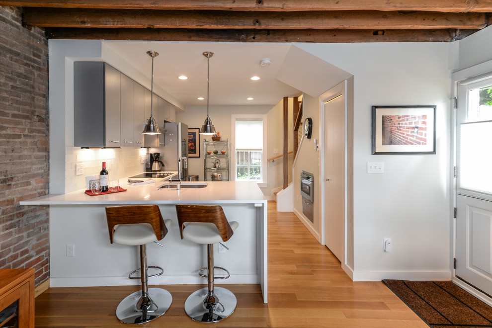 Foto på ett litet rustikt vit kök, med mellanmörkt trägolv, brunt golv, en undermonterad diskho, släta luckor, grå skåp, bänkskiva i kvarts, vitt stänkskydd, stänkskydd i glaskakel, rostfria vitvaror och en halv köksö