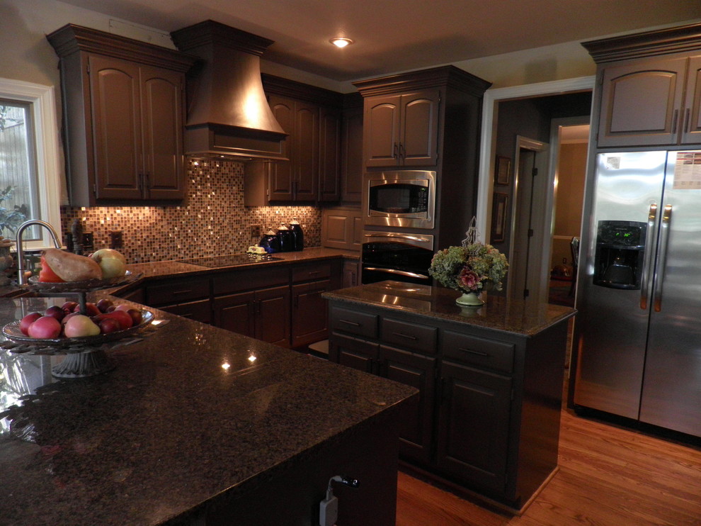 Example of a classic u-shaped light wood floor kitchen design in Kansas City with an undermount sink, recessed-panel cabinets, brown cabinets, multicolored backsplash, glass sheet backsplash, stainless steel appliances and an island