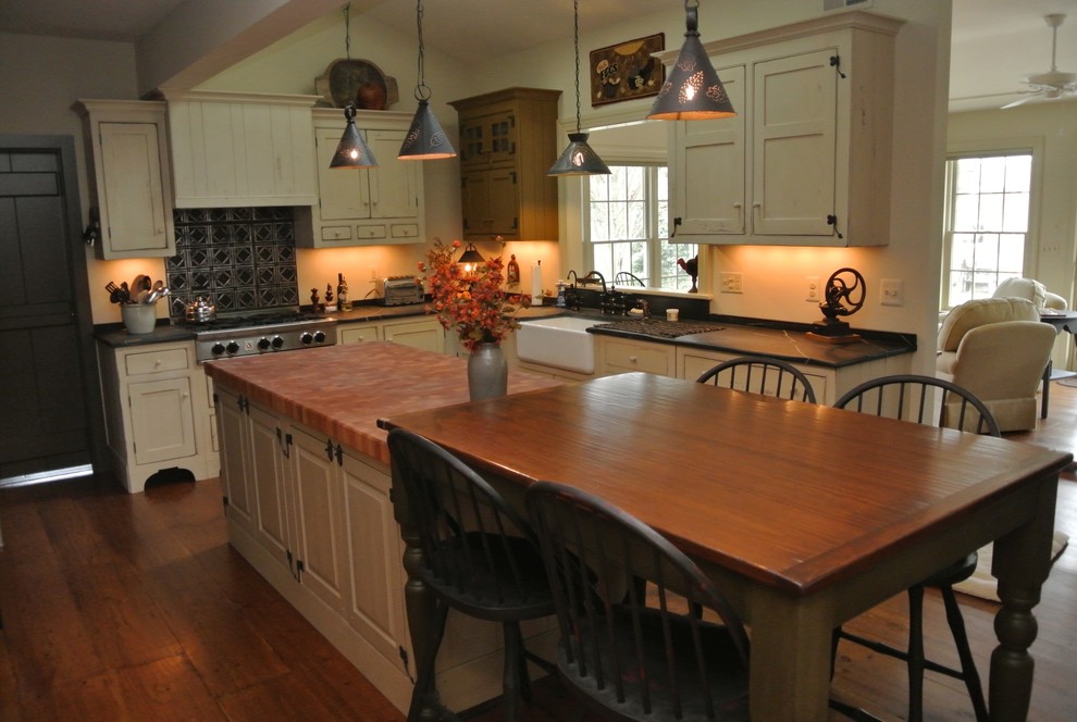 Example of a large cottage l-shaped medium tone wood floor open concept kitchen design in New York with a farmhouse sink, recessed-panel cabinets, beige cabinets, soapstone countertops, black backsplash, stainless steel appliances and an island