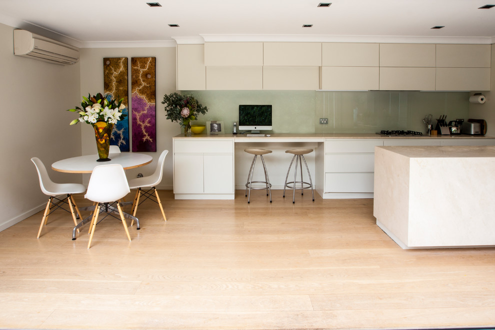 Bild på ett mellanstort funkis linjärt kök och matrum, med en dubbel diskho, släta luckor, vita skåp, marmorbänkskiva, vitt stänkskydd, glaspanel som stänkskydd, rostfria vitvaror, ljust trägolv och en köksö