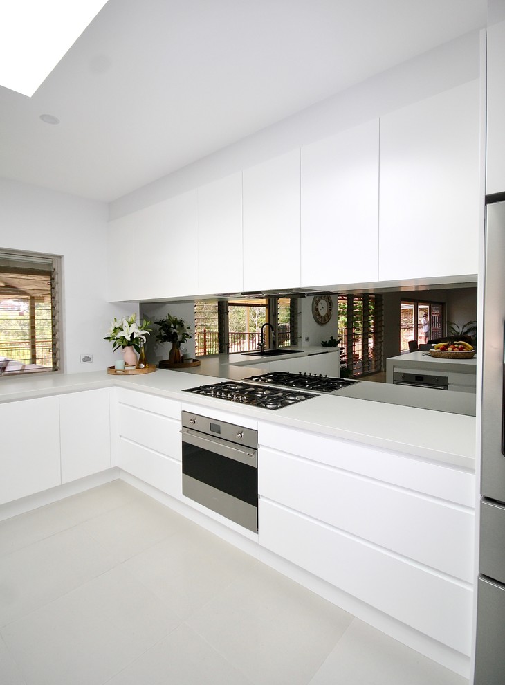 Example of a large minimalist l-shaped ceramic tile and gray floor eat-in kitchen design in Sydney with a drop-in sink, flat-panel cabinets, white cabinets, quartz countertops, gray backsplash, mirror backsplash, stainless steel appliances, an island and gray countertops