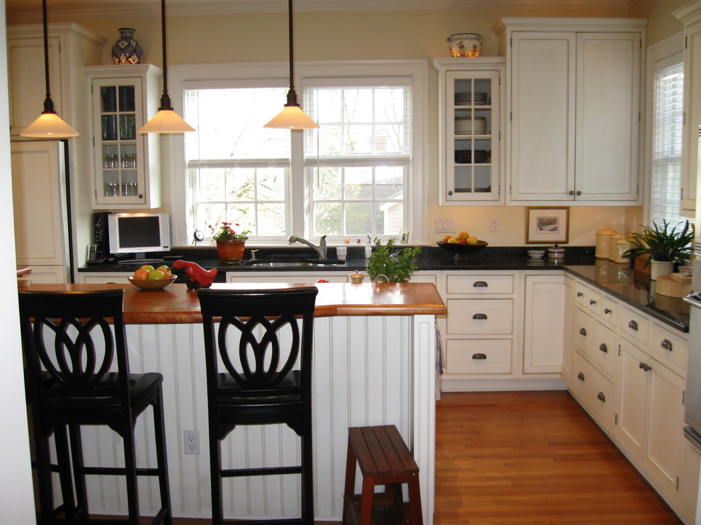 Inredning av ett klassiskt mellanstort kök, med en undermonterad diskho, luckor med infälld panel, vita skåp, granitbänkskiva, svart stänkskydd, stänkskydd i sten, vita vitvaror, mellanmörkt trägolv, en köksö och brunt golv