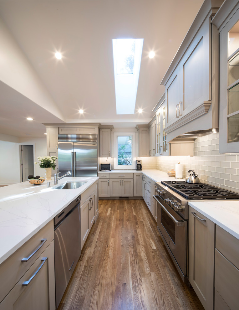 Mid-sized elegant u-shaped medium tone wood floor and brown floor eat-in kitchen photo in Baltimore with an undermount sink, shaker cabinets, gray cabinets, marble countertops, white backsplash, glass tile backsplash, stainless steel appliances and an island