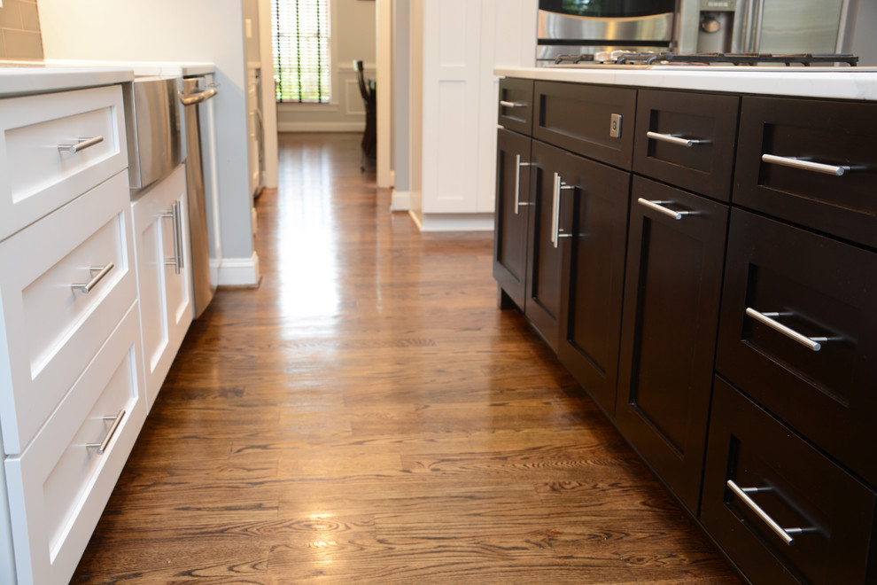 Mid-sized transitional l-shaped dark wood floor and brown floor eat-in kitchen photo in Baltimore with a farmhouse sink, shaker cabinets, white cabinets, quartz countertops, brown backsplash, glass tile backsplash, stainless steel appliances, an island and white countertops