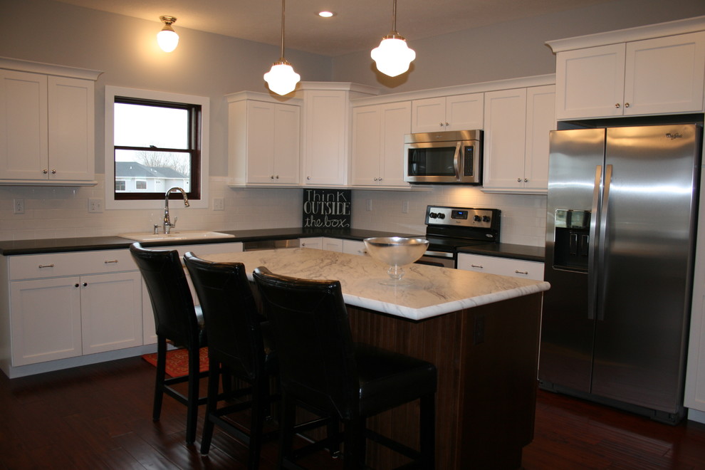 Bild på ett mellanstort lantligt kök, med en dubbel diskho, skåp i shakerstil, vita skåp, granitbänkskiva, vitt stänkskydd, stänkskydd i keramik, rostfria vitvaror, mörkt trägolv, en köksö och brunt golv