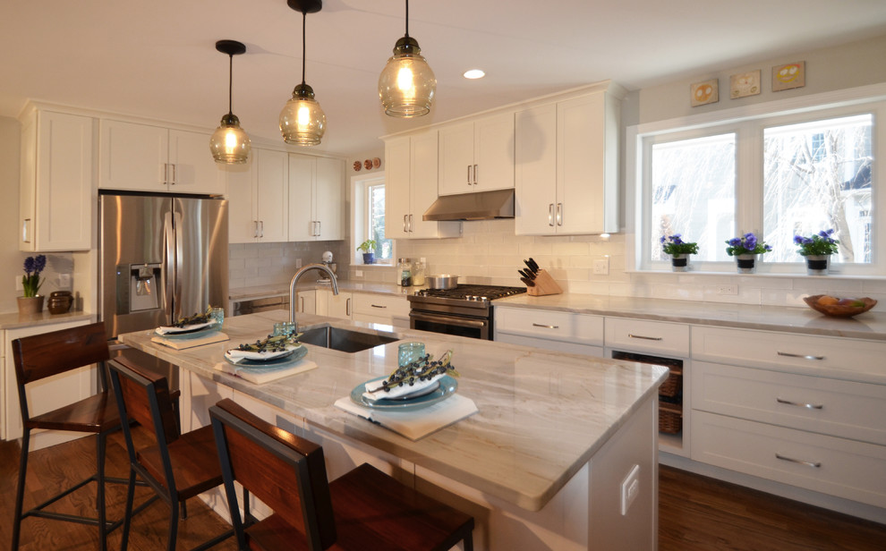 Example of a large transitional u-shaped medium tone wood floor open concept kitchen design in DC Metro with an undermount sink, shaker cabinets, white cabinets, quartzite countertops, white backsplash, glass tile backsplash, stainless steel appliances and an island