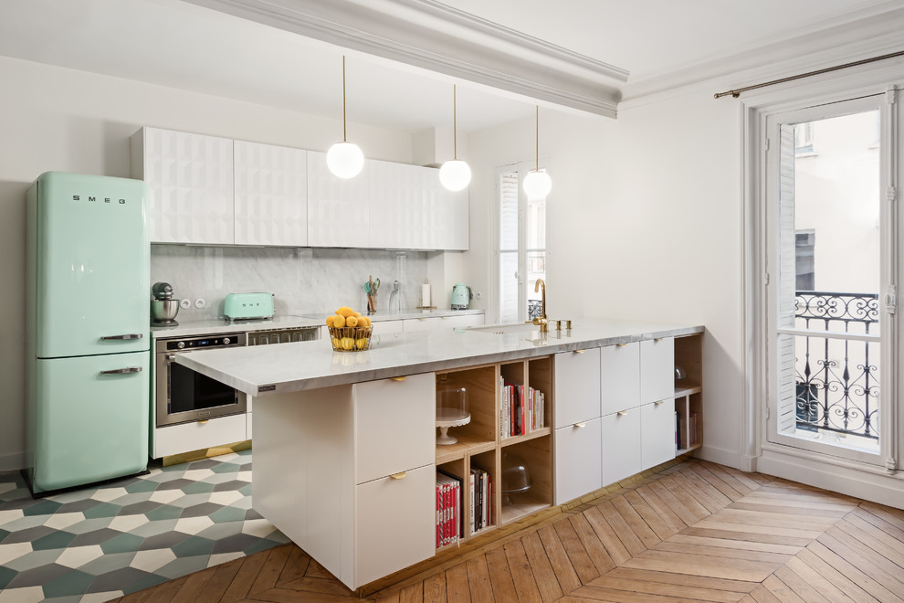 Example of a mid-sized eclectic galley medium tone wood floor and brown floor kitchen design in Essex with a farmhouse sink, flat-panel cabinets, white cabinets, marble countertops, gray backsplash, marble backsplash, stainless steel appliances and an island