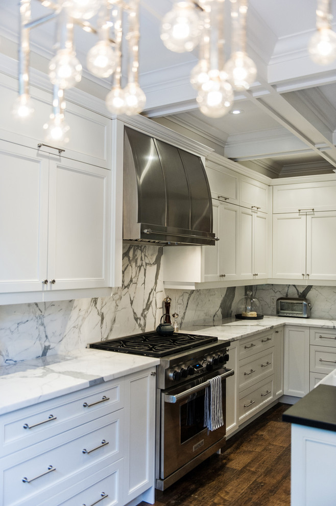 Photo of a large contemporary l-shaped open plan kitchen in Toronto with a belfast sink, recessed-panel cabinets, white cabinets, marble worktops, white splashback, marble splashback, stainless steel appliances, medium hardwood flooring, an island, brown floors and white worktops.