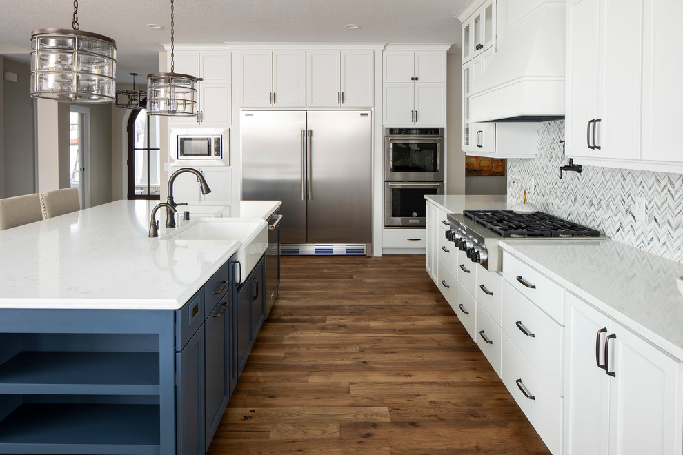 Photo of a traditional u-shaped kitchen in Minneapolis with a belfast sink, shaker cabinets, white cabinets, stainless steel appliances, medium hardwood flooring, an island, brown floors and white worktops.