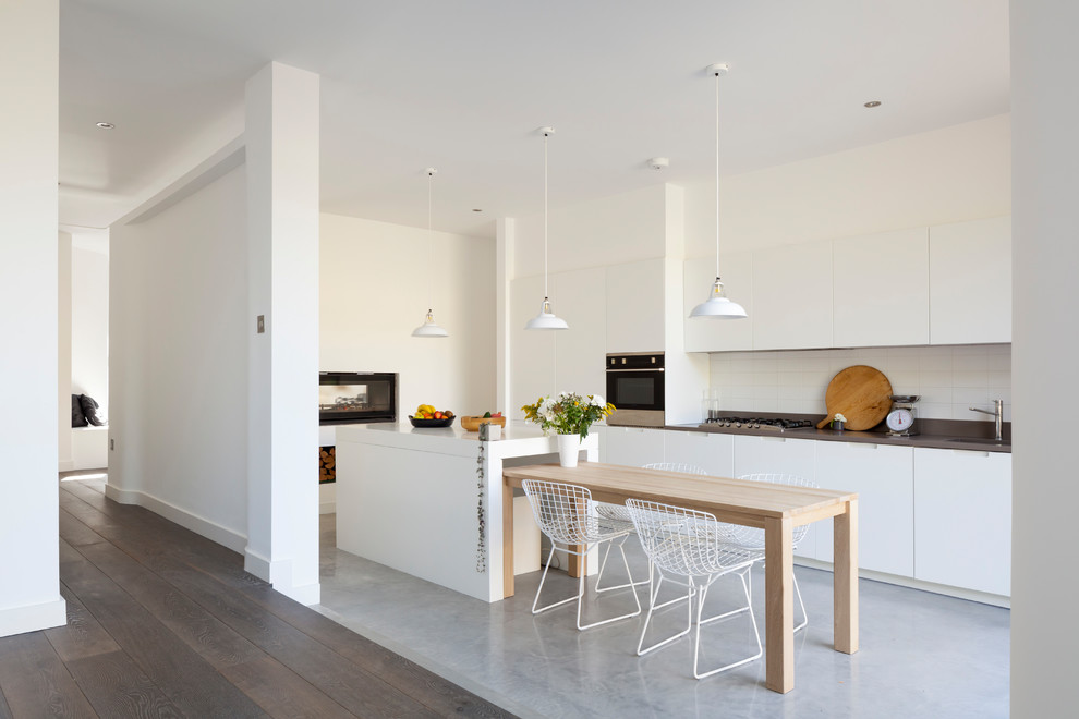Inredning av ett modernt mellanstort linjärt kök och matrum, med en nedsänkt diskho, släta luckor, vita skåp, stänkskydd i tunnelbanekakel, rostfria vitvaror, betonggolv, en köksö och flerfärgat golv