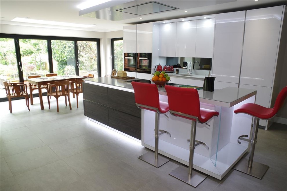 Пример оригинального дизайна: кухня в стиле модернизм с обеденным столом, белыми фасадами, черной техникой, полуостровом, серым полом и серой столешницей