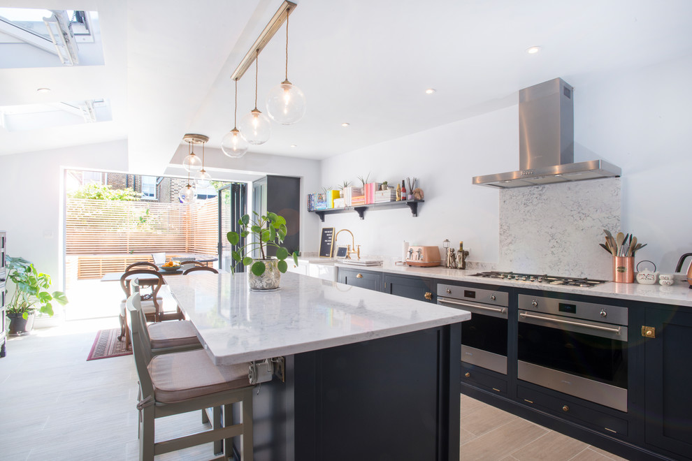 Medium sized modern single-wall kitchen/diner in London with a belfast sink, recessed-panel cabinets, blue cabinets, stainless steel appliances, an island and white worktops.