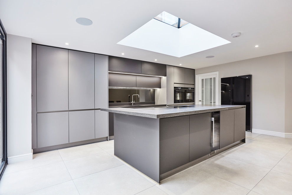 Idéer för mellanstora funkis linjära grått kök med öppen planlösning, med en integrerad diskho, släta luckor, grå skåp, bänkskiva i kvartsit, stänkskydd med metallisk yta, spegel som stänkskydd, svarta vitvaror, klinkergolv i porslin, en köksö och grått golv
