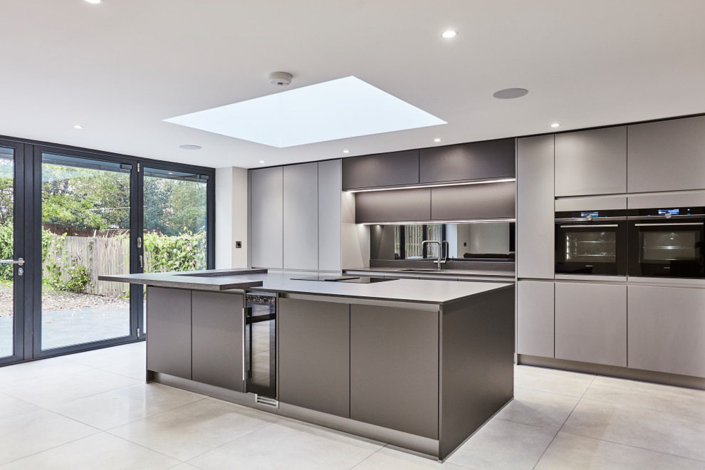This is an example of a medium sized contemporary single-wall open plan kitchen in Other with an integrated sink, flat-panel cabinets, grey cabinets, quartz worktops, metallic splashback, mirror splashback, black appliances, porcelain flooring, an island, grey floors, grey worktops and a vaulted ceiling.