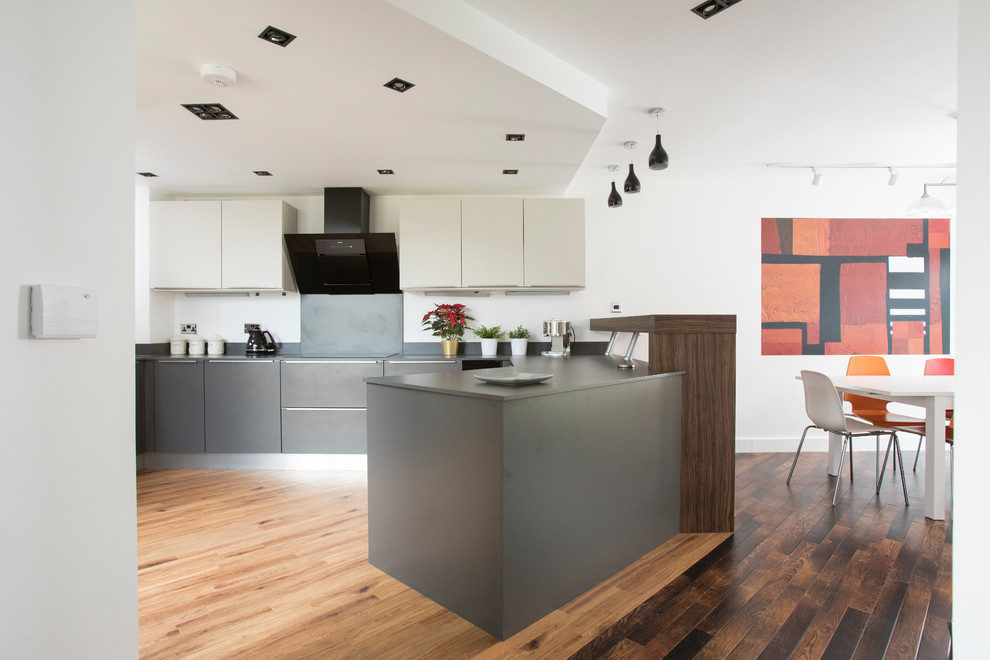 Photo of a contemporary u-shaped kitchen/diner in Other with flat-panel cabinets, grey cabinets, laminate countertops, grey splashback, stainless steel appliances, medium hardwood flooring, a breakfast bar, brown floors and grey worktops.