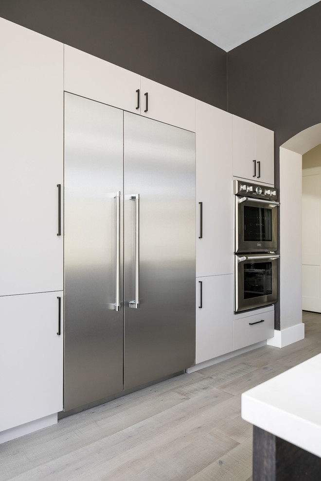 Inspiration for a large contemporary l-shaped open plan kitchen in Phoenix with a belfast sink, flat-panel cabinets, engineered stone countertops, white splashback, metro tiled splashback, stainless steel appliances, light hardwood flooring, an island, grey floors and white worktops.