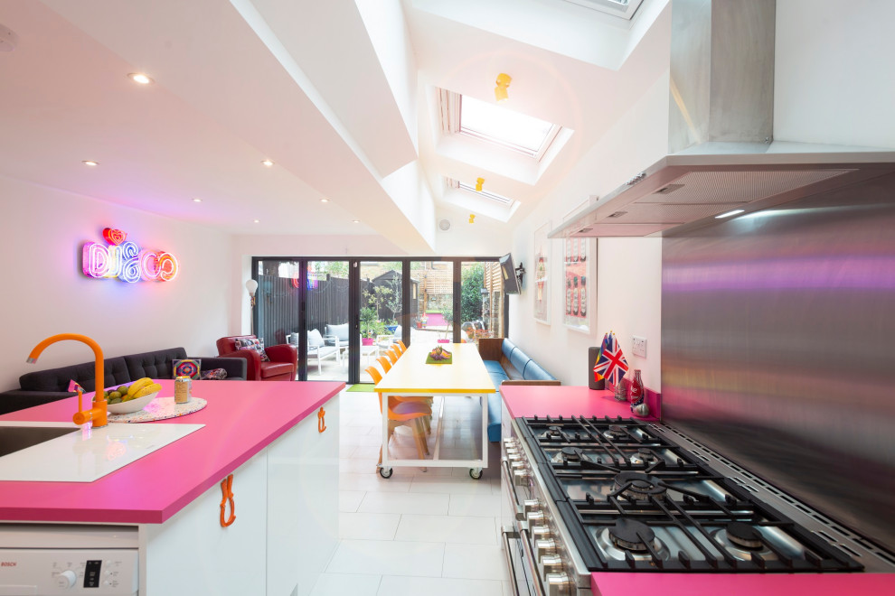 Photo of a medium sized bohemian l-shaped open plan kitchen in London with an integrated sink, flat-panel cabinets, white cabinets, composite countertops, pink splashback, stainless steel appliances, ceramic flooring, an island, white floors and pink worktops.