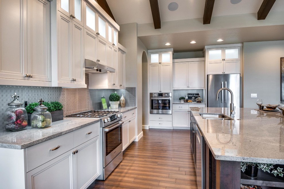 Inspiration for a large contemporary l-shaped vinyl floor and brown floor open concept kitchen remodel in Boise with a double-bowl sink, recessed-panel cabinets, white cabinets, gray backsplash, glass tile backsplash, stainless steel appliances and an island