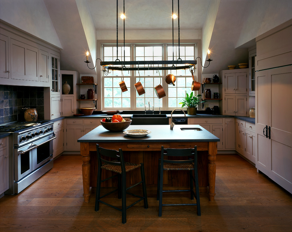 Inredning av ett stort kök, med en rustik diskho, skåp i shakerstil, grå skåp, bänkskiva i täljsten, grått stänkskydd, stänkskydd i stenkakel, integrerade vitvaror, mellanmörkt trägolv och en köksö