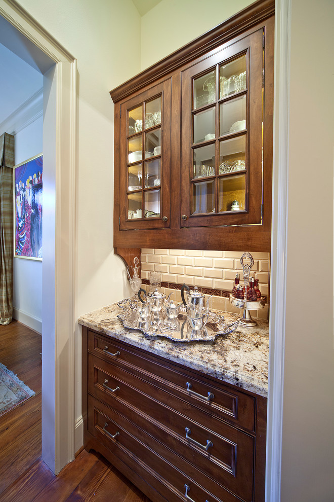 Klassisk inredning av ett avskilt, mellanstort linjärt kök, med luckor med glaspanel, granitbänkskiva, bruna skåp, vitt stänkskydd, stänkskydd i tunnelbanekakel, mellanmörkt trägolv och brunt golv
