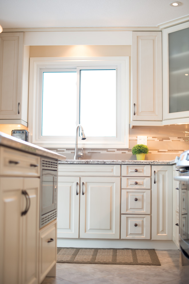 This is an example of a classic kitchen in Toronto with a double-bowl sink, raised-panel cabinets, white cabinets, granite worktops, beige splashback, glass tiled splashback, stainless steel appliances, vinyl flooring and an island.