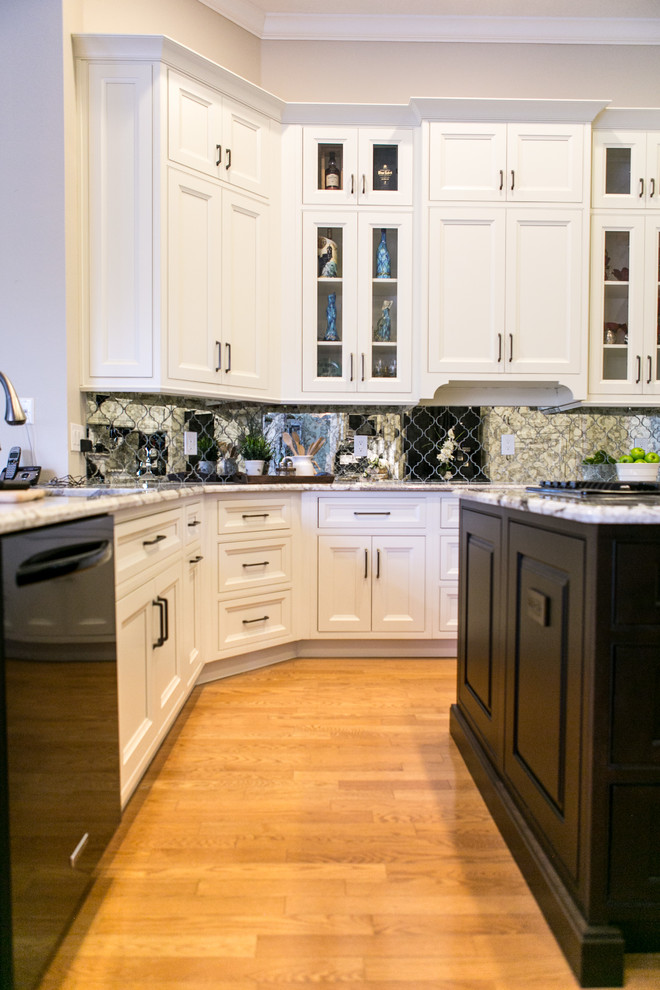 Inredning av ett klassiskt mellanstort kök, med en undermonterad diskho, luckor med infälld panel, vita skåp, granitbänkskiva, spegel som stänkskydd, svarta vitvaror, ljust trägolv, en köksö och brunt golv