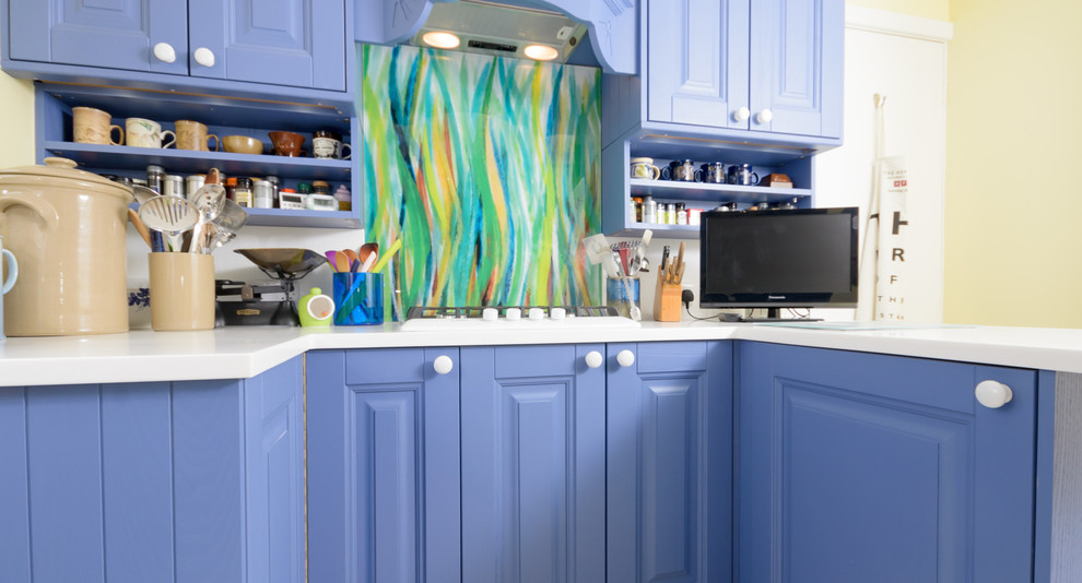 Ejemplo de cocina ecléctica pequeña abierta con puertas de armario azules, encimera de madera, salpicadero multicolor, salpicadero de vidrio templado y suelo laminado