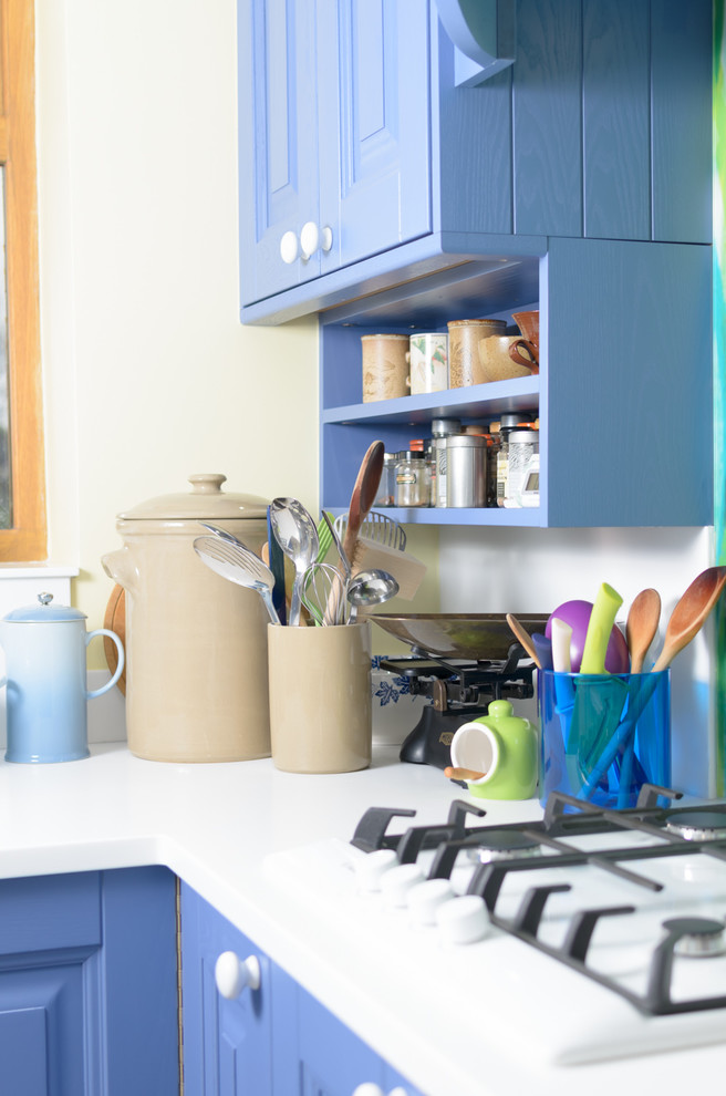 Modelo de cocina ecléctica pequeña abierta con puertas de armario azules, encimera de madera, salpicadero multicolor, salpicadero de vidrio templado y suelo laminado