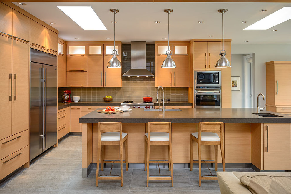 Photo of a contemporary grey and cream kitchen in Vancouver with flat-panel cabinets, stainless steel appliances, light wood cabinets, glass tiled splashback and grey splashback.