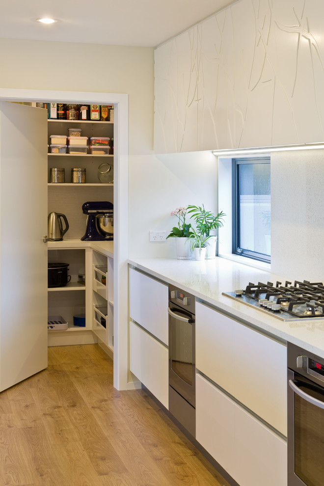 Cette photo montre une cuisine moderne avec un placard à porte plane, des portes de placard blanches et un sol en bois brun.
