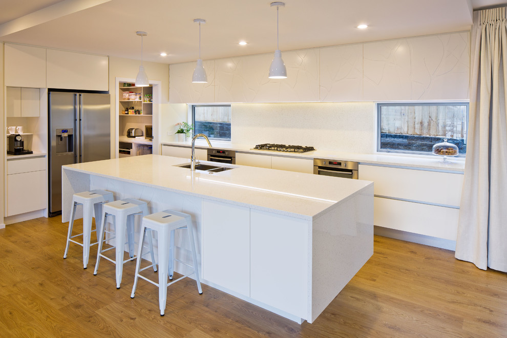 Moderne Küche in L-Form mit Doppelwaschbecken, flächenbündigen Schrankfronten, weißen Schränken, Küchengeräten aus Edelstahl, braunem Holzboden und Kücheninsel in Wellington