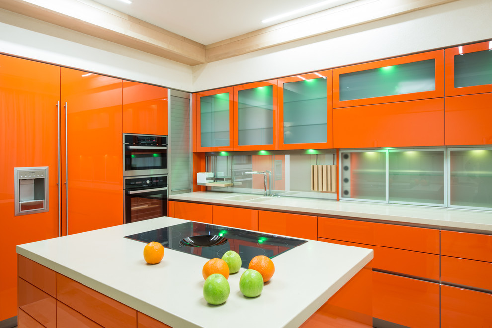 На фото: угловая, глянцевая кухня в современном стиле с плоскими фасадами, оранжевыми фасадами, техникой под мебельный фасад и островом с