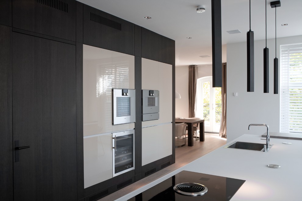 Modelo de cocina moderna de tamaño medio con armarios tipo vitrina, puertas de armario blancas, encimera de vidrio, electrodomésticos de acero inoxidable y una isla