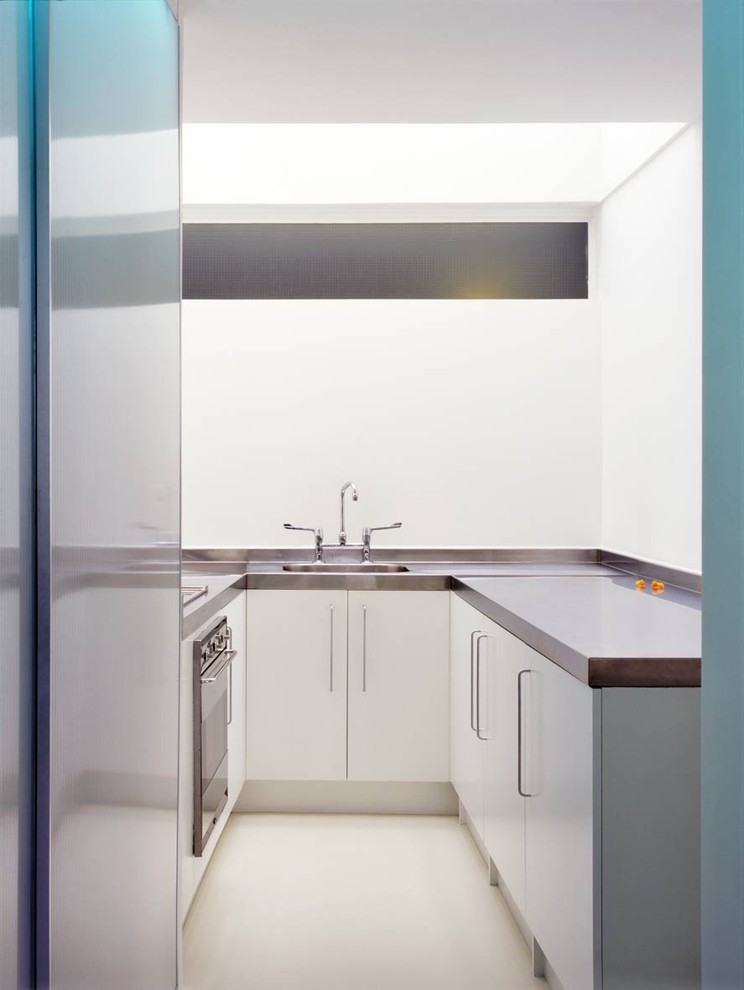 Example of a minimalist u-shaped enclosed kitchen design in London with stainless steel countertops, an integrated sink, flat-panel cabinets, white cabinets and stainless steel appliances