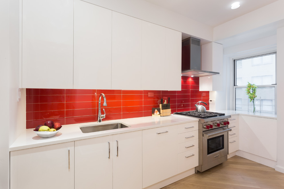Bild på ett mellanstort funkis kök, med en undermonterad diskho, släta luckor, vita skåp, bänkskiva i koppar, rött stänkskydd, stänkskydd i glaskakel, rostfria vitvaror och ljust trägolv