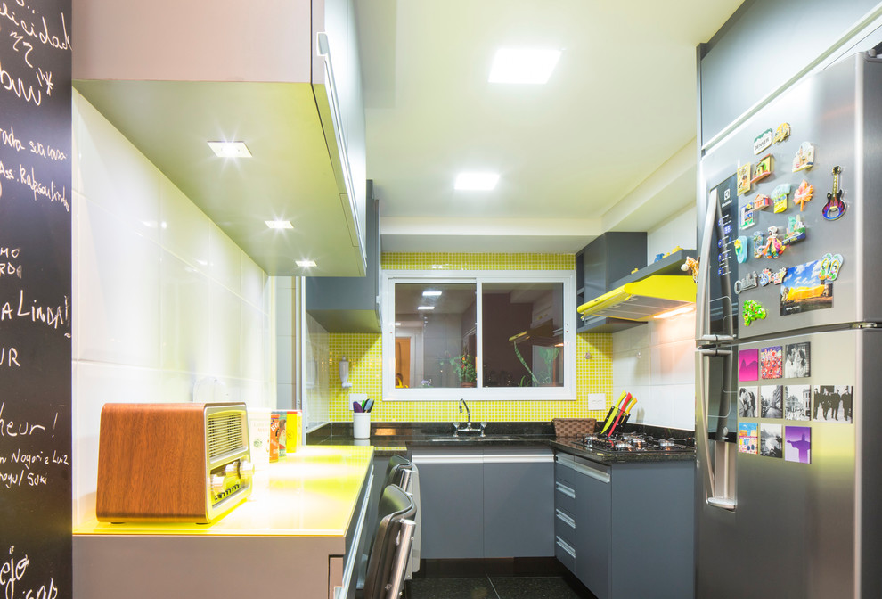 他の地域にある高級な小さなコンテンポラリースタイルのおしゃれなキッチン (ダブルシンク、フラットパネル扉のキャビネット、グレーのキャビネット、御影石カウンター、黄色いキッチンパネル、ガラスタイルのキッチンパネル、磁器タイルの床) の写真