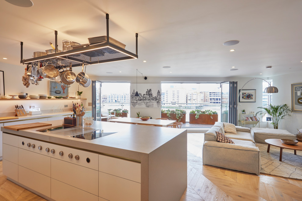 This is an example of an open plan kitchen in London with flat-panel cabinets, beige cabinets, composite countertops, stainless steel appliances, medium hardwood flooring, an island, beige floors and beige worktops.