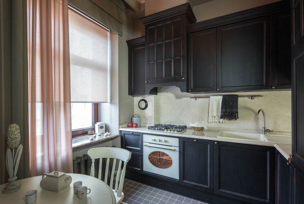 Inredning av ett klassiskt kök, med svarta skåp, vitt stänkskydd, vita vitvaror, grått golv, en nedsänkt diskho och luckor med infälld panel