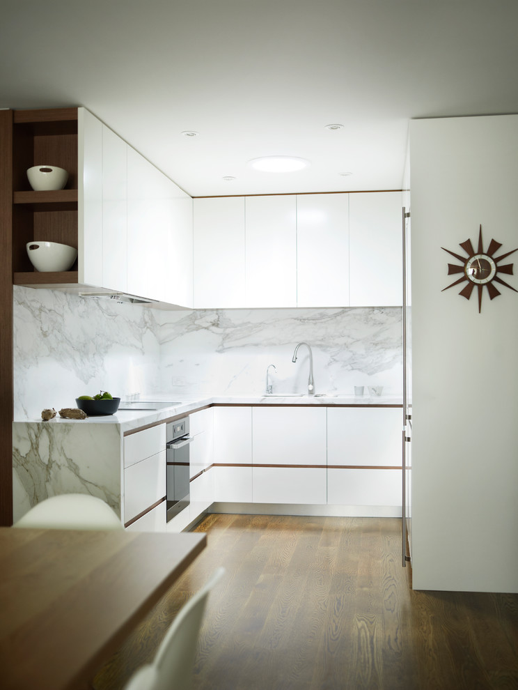 Inredning av ett modernt litet u-kök, med vita skåp, marmorbänkskiva, vitt stänkskydd, integrerade vitvaror, mörkt trägolv och stänkskydd i marmor