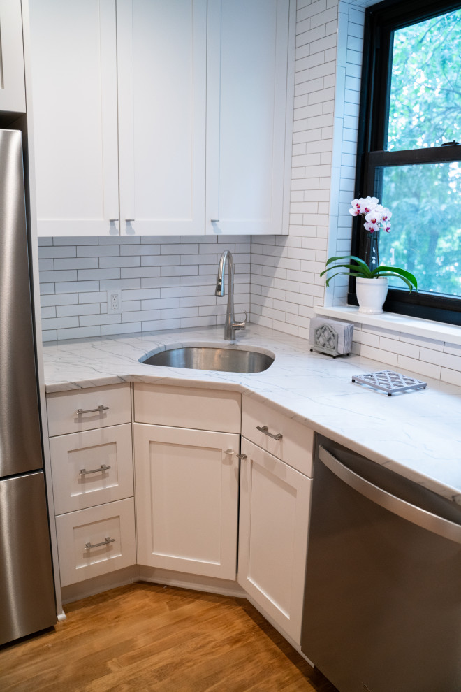 Inredning av ett modernt litet vit vitt kök, med en enkel diskho, skåp i shakerstil, vita skåp, bänkskiva i kvartsit, vitt stänkskydd, stänkskydd i tunnelbanekakel, rostfria vitvaror, mellanmörkt trägolv, en köksö och brunt golv