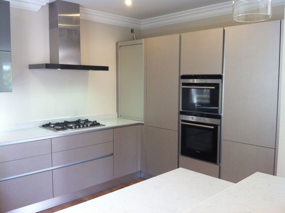 Bild på ett mellanstort funkis kök, med en dubbel diskho, släta luckor, grå skåp, bänkskiva i kvarts, vitt stänkskydd, spegel som stänkskydd, rostfria vitvaror, mörkt trägolv och en halv köksö