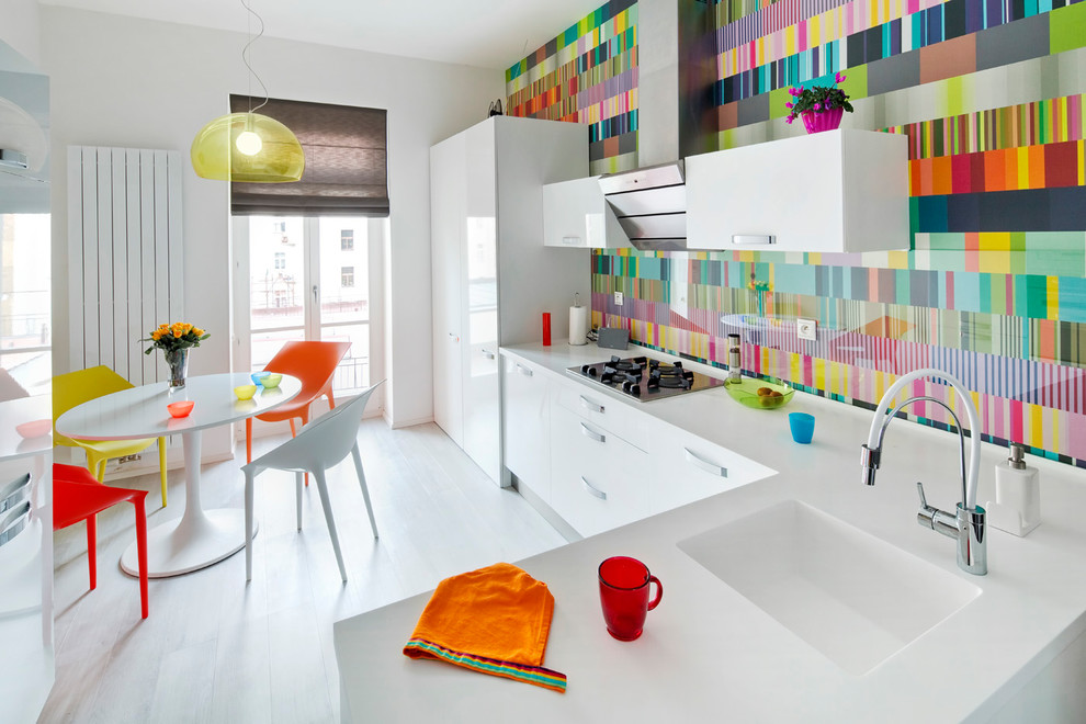 Design ideas for a contemporary l-shaped kitchen/diner in Other with an integrated sink, flat-panel cabinets, white cabinets, multi-coloured splashback, glass sheet splashback, white appliances, white floors and white worktops.