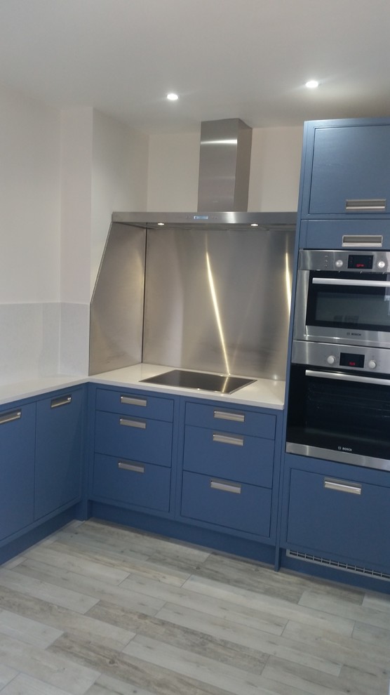 Photo of a medium sized contemporary l-shaped enclosed kitchen in London with a built-in sink, flat-panel cabinets, blue cabinets, quartz worktops, white splashback, stainless steel appliances and ceramic flooring.