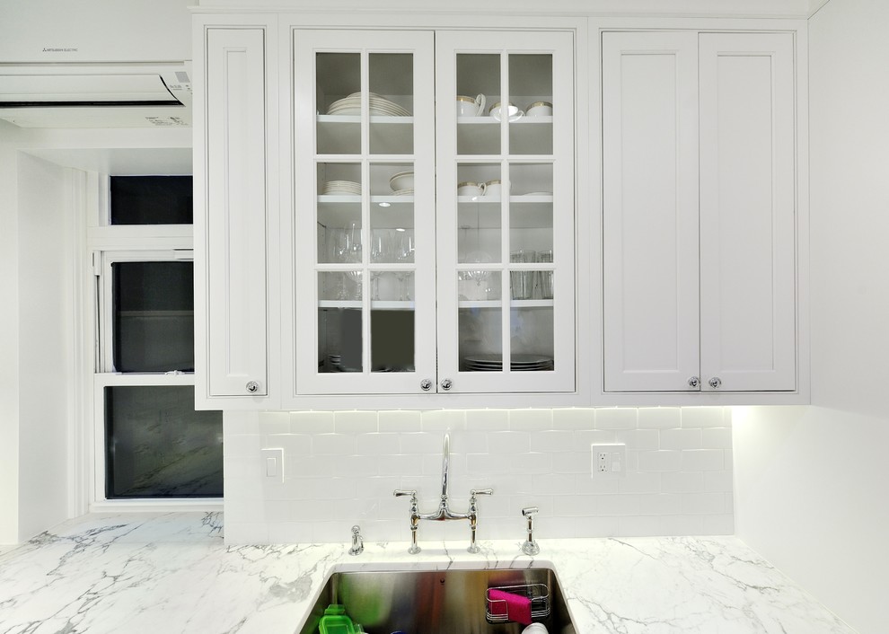 ニューヨークにある中くらいなコンテンポラリースタイルのおしゃれなキッチン (シングルシンク、落し込みパネル扉のキャビネット、白いキャビネット、大理石カウンター、白いキッチンパネル、セラミックタイルのキッチンパネル、シルバーの調理設備、濃色無垢フローリング) の写真